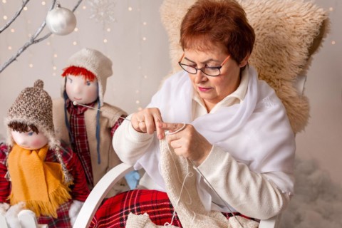 A nice elderly woman sews to knit her granddaughters in a Christmas arrangement. In studio