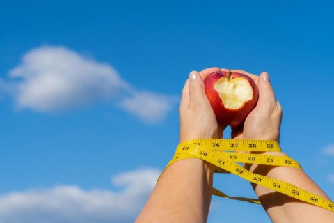 Woman holding a bitten apple in her hands with a tape measure and a sky with clouds in the background