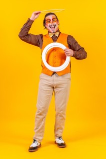 Happy juggler man in makeup vest juggling hoops on a yellow background