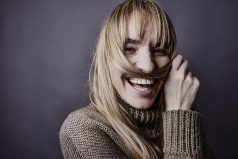 Young woman with long blond hair makes a moustache out of a strand of hair and smiles at camera