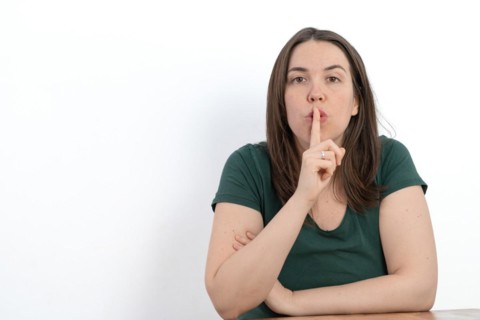 Close-up of young long-haired woman with finger in mouth asking for silence white background