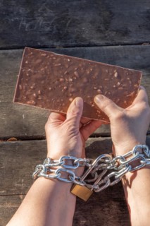 Woman holding a chocolate bar with her hands chained together as a dietary slave concept