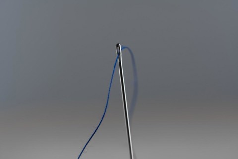 Sewing needle and blue thread against a neutral background