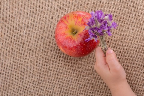 Hand holding a flower bouquet beside an apple