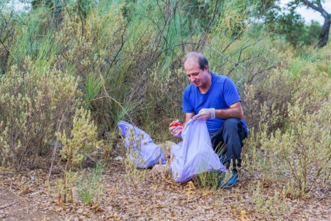 Environmentalist man with garbage bags picking up garbage from the field and taking care of the environment
