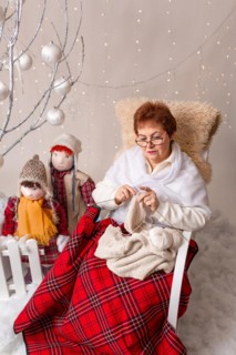 A nice elderly woman sews to knit her granddaughters in a Christmas arrangement. In studio