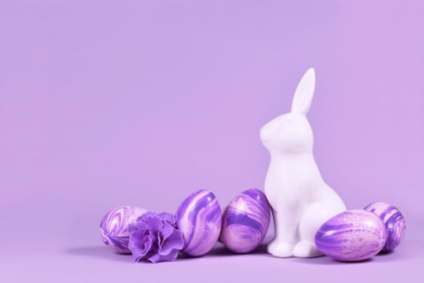 Easter eggs next to bunny figure on violet background