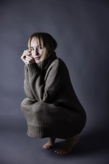 Squatting young woman with long blond hair has pulled knitted jumper over her knees