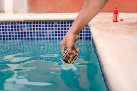 Close up of person testing the ph of the water with mini tester in swimming pool. Hand testing pool water for chlorine with PH mini tester. Testing the chlorine and PH of swimming pool