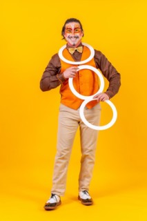 Happy juggler man in makeup vest juggling hoops on a yellow background