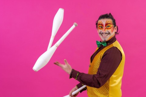 Clown with white facial makeup on a pink background