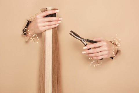 Hands with flowers hold strands of hair for extensions on a beige background. hair beauty