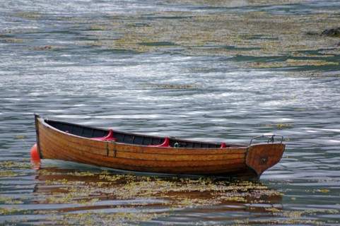 Small wooden rowing boat lying in the shallow waters of Plockton Harbour