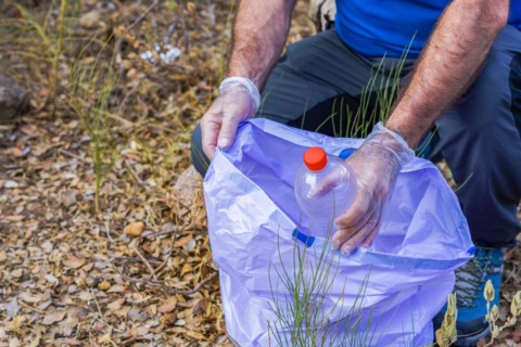 Environmentalist man with garbage bags picking up garbage from the field and taking care of the environment