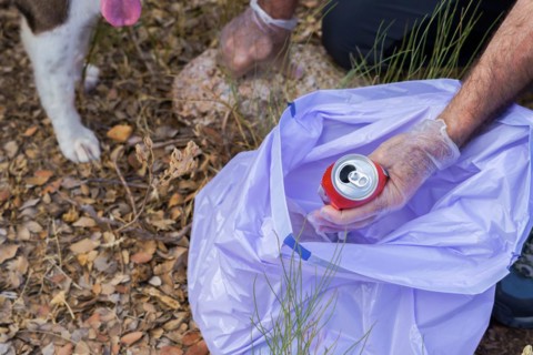 Environmentalist man with his dog throwing a can picked up in the field into a garbage bag