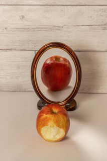 Bitten red apple reflected in a mirror isolated on a white table with copy space