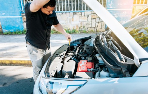 Man checking the oil in his vehicle. Person checking the oil level of his car in the street. Driver inspecting car oil level