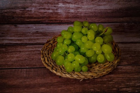 Close-up of a bunch of green grapes on an esparto grass tray with a dark wood background