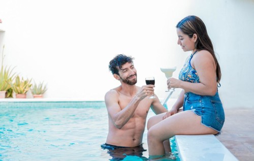 Smiling couple enjoying and toasting in swimming pool. Young man and woman on vacation toasting in the pool