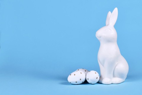 Easter bunny and white and gold Easter eggs with dots on blue background with copy space