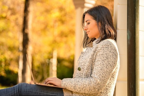 Pretty woman with glasses and MacBook in hand sits in the park at autumn time