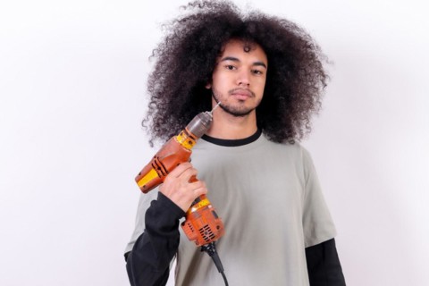 Portrait of the technician with the drill. Young man with afro hair on white background