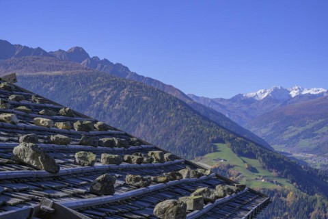 Shingle roof weighted down with stones behind it snow-covered mountains above the Ulten Valley seen from the Pfrollnhof wine tavern