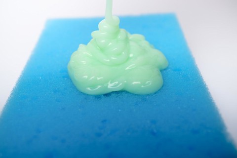 Green liquid soap dripping on a blue sponge on a white background