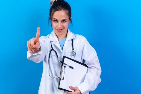 Portrait of smiling female doctor in medical gown standing isolated on blue