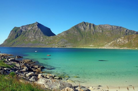 Crystal clear sea bay with small boat and rugged green mountains