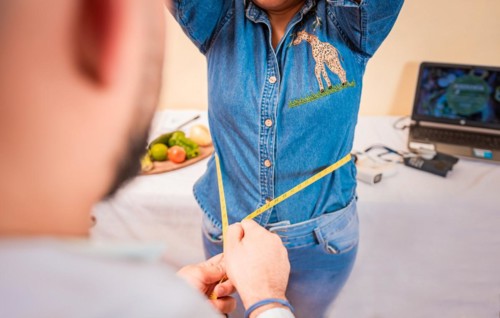 Close-up of nutritionist measuring waist to patient. View of a male nutritionist measuring female patient waist. Concept of weight loss and professional nutritionist