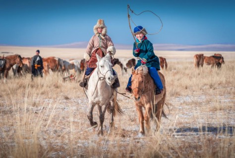 Happy children riding horses in winter. Dornod Province. Mongolia