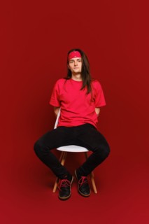 Young adult man in black and red casual clothes sits on chair with his arms behind back