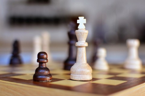 Chess board game with focus on white queen pieces on blurry background