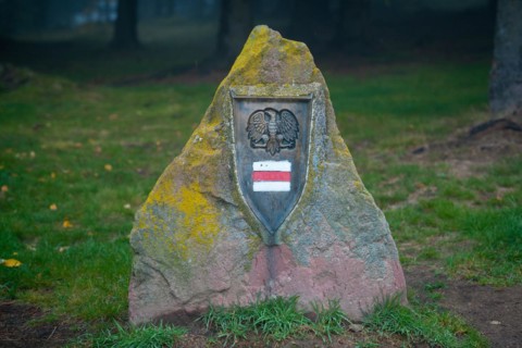A large obelisk is placed next to the tourist trail with a trail sign and an eagle on it. Polish mountains