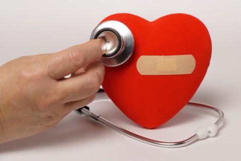 Woman auscultating a red heart with a band-aid with a stethoscope isolated on a white background