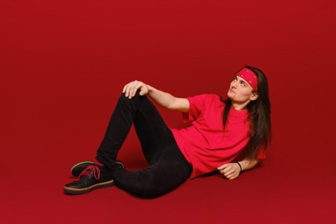 Active young man with long hair and head band sitting on floor in red studio
