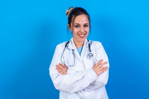 Portrait of smiling female doctor in medical gown standing isolated on blue
