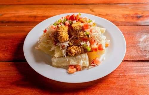 Traditional chicharron dish with cassava and tomato salad. Latin food chicharron con yuca served on wooden table. Nicaraguan dish chicharron with cassava on the table