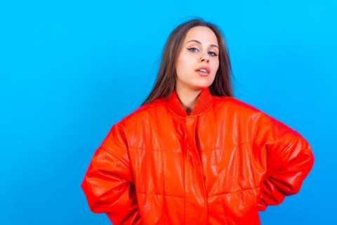 Close up portrait of young caucasian woman in red windbreaker isolated on blue background