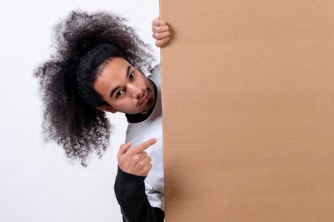 Smiling holding a sign with copy paste space. Young man with afro hair on white background