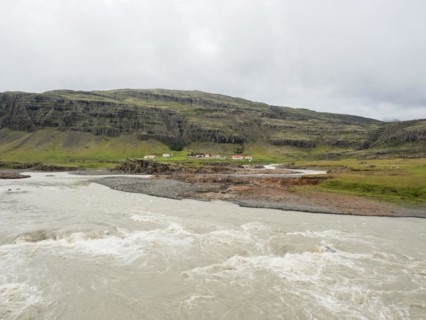 Glacier river and farm in front of mountain range