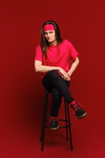Young adult man sits on high stool with his leg on another leg and leaning forward