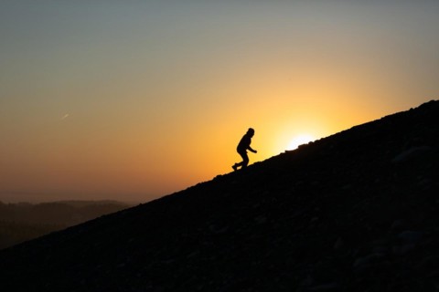 Silhouette of man is climbing to peak of hill with sunset or sunrise background. Poland