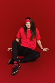 Active young man with long hair and head band sitting on floor in red studio