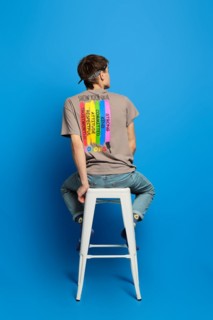 Unrecognizable adult person sits on tall stool in t-shirt with rainbow flag printed on back side. Concept of tolerant attitude to lgbt people