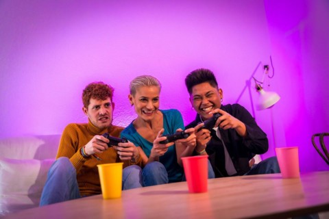 Group of young friends playing video games together on the sofa at home, purple led, racing game
