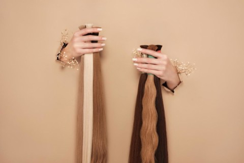 Hands with flowers hold strands of hair for extensions on a beige background. hair beauty