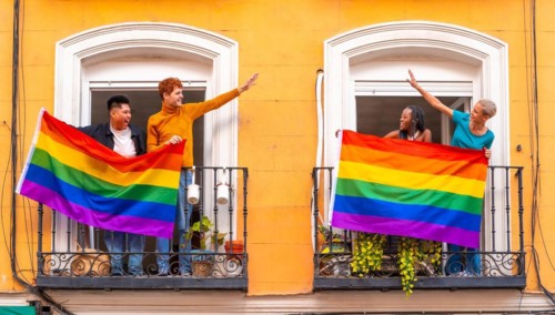 Couples of gay boys and lesbian girls with the lgtb flag on the balconies at a house party, greeting friends, LGBT pride