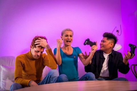 Group of young friends playing video games together on the sofa at home, purple led, woman winning